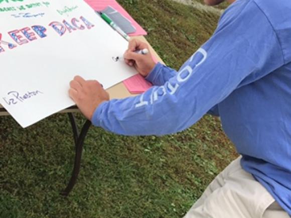 Student Signs DACA Poster on the campus green