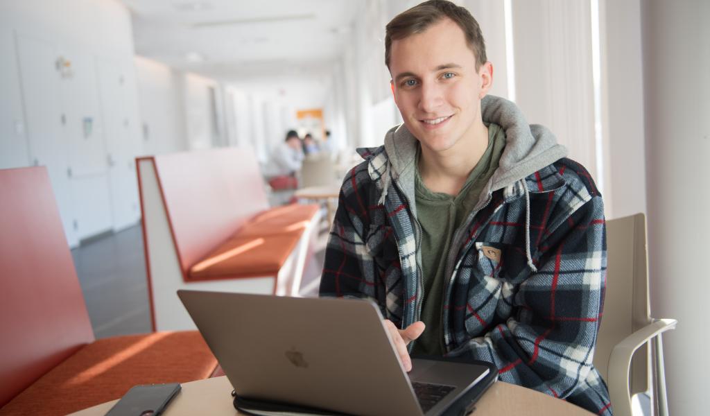 Male student looks at thew camera as he sits in front of his laptop in the Stevens Center